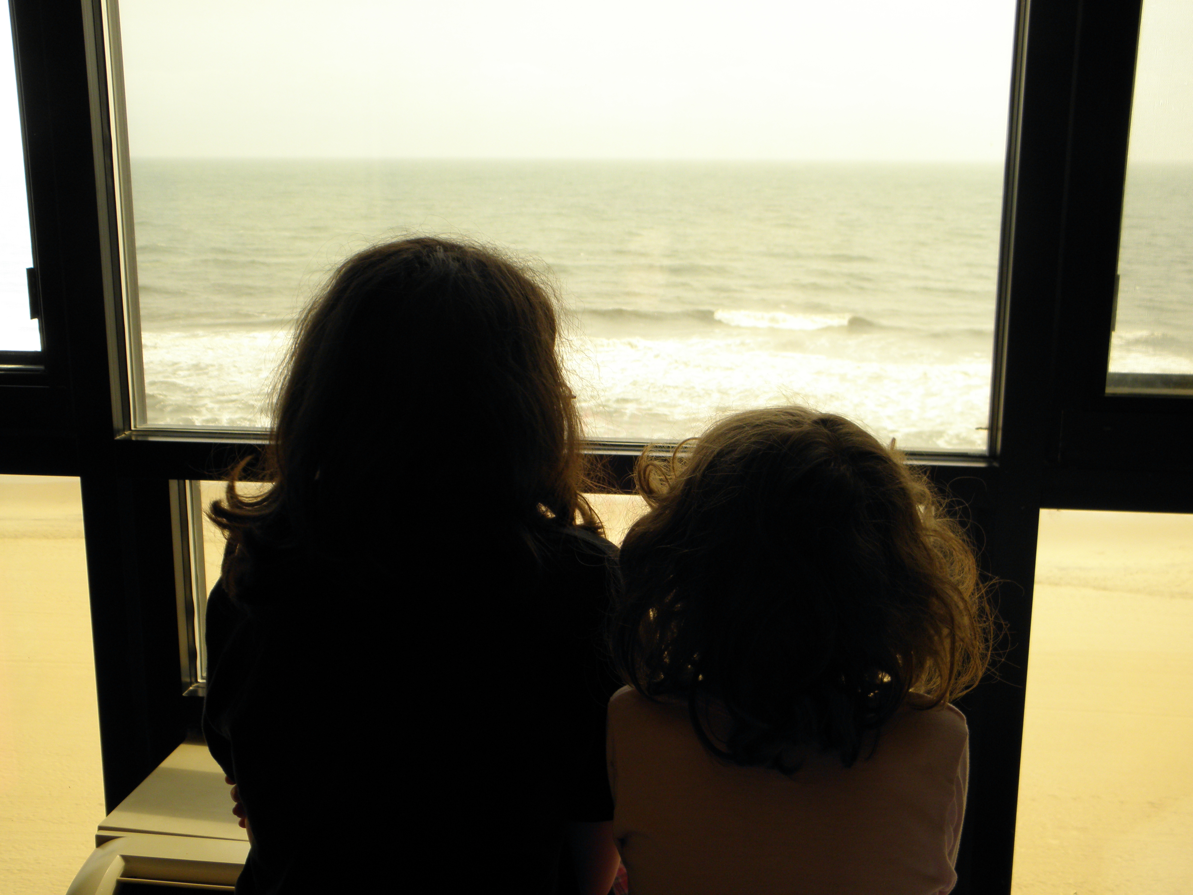 Two girls looking out the window at the beach.