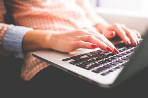 Woman's hands typing on laptop on her lap.
