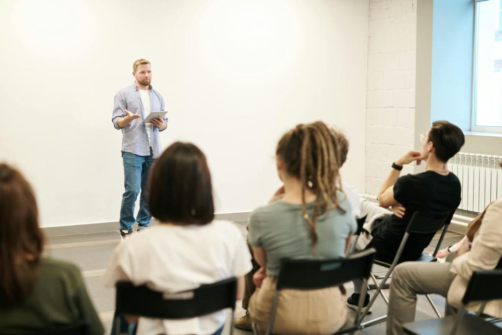 A man in blue jeans and a blue shirt speaking in front of a small group of people seated in folding chairs.
